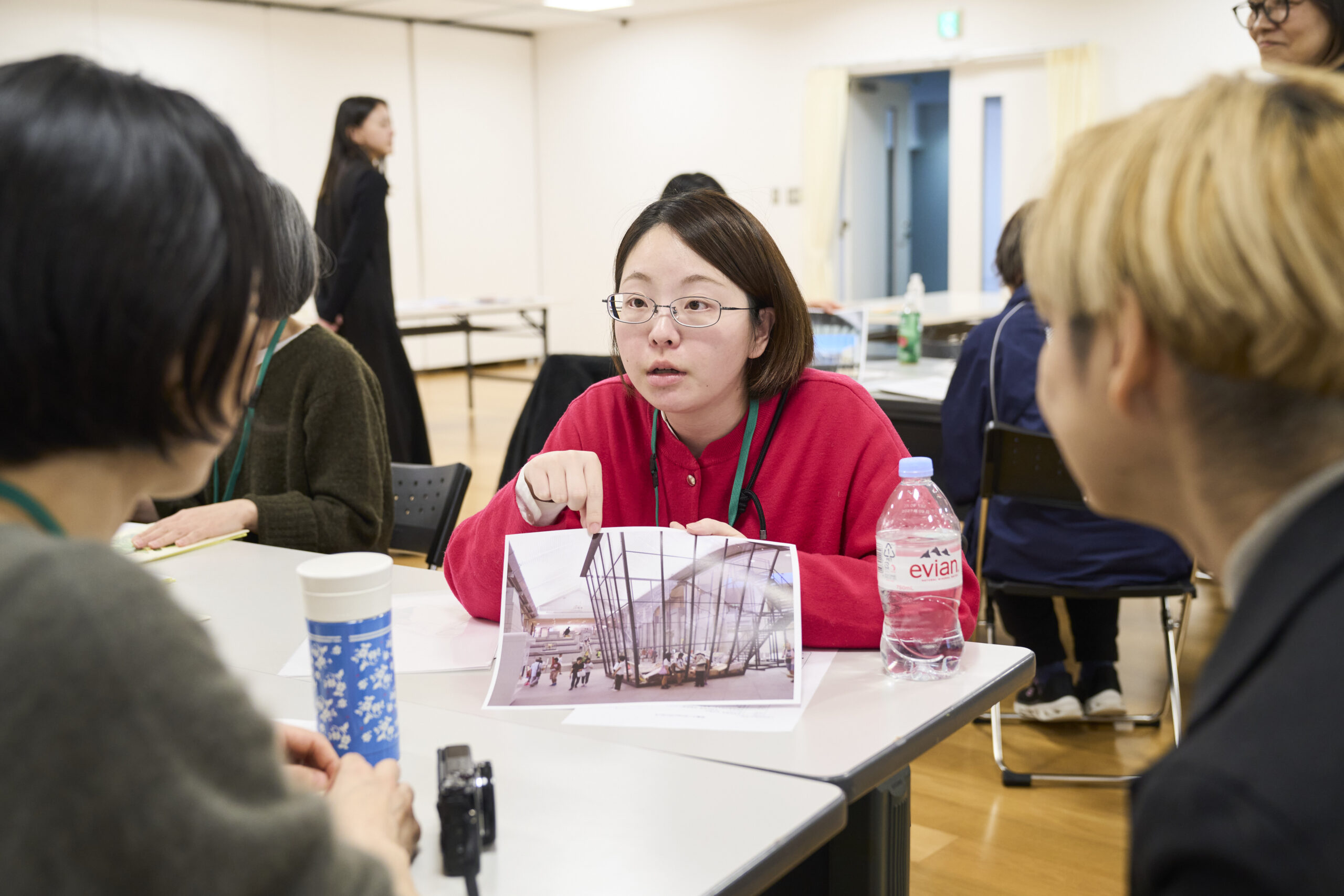 3人の人物が向き合って話している。中央の人物が、手に写真を持ちながら指を指して話している。