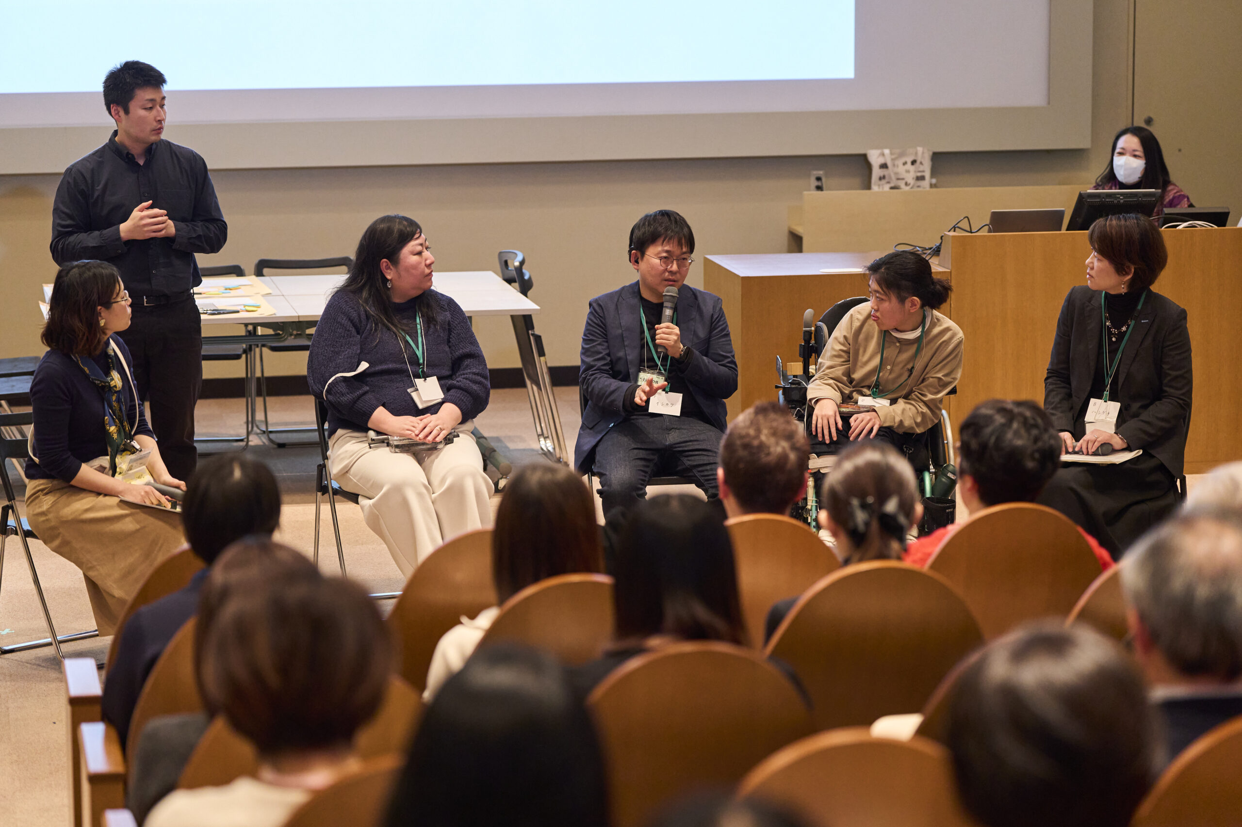 5名の人物が前に座っており、客席から複数の人物が話しを聞いている。中央の人物がマイクを持って話している。